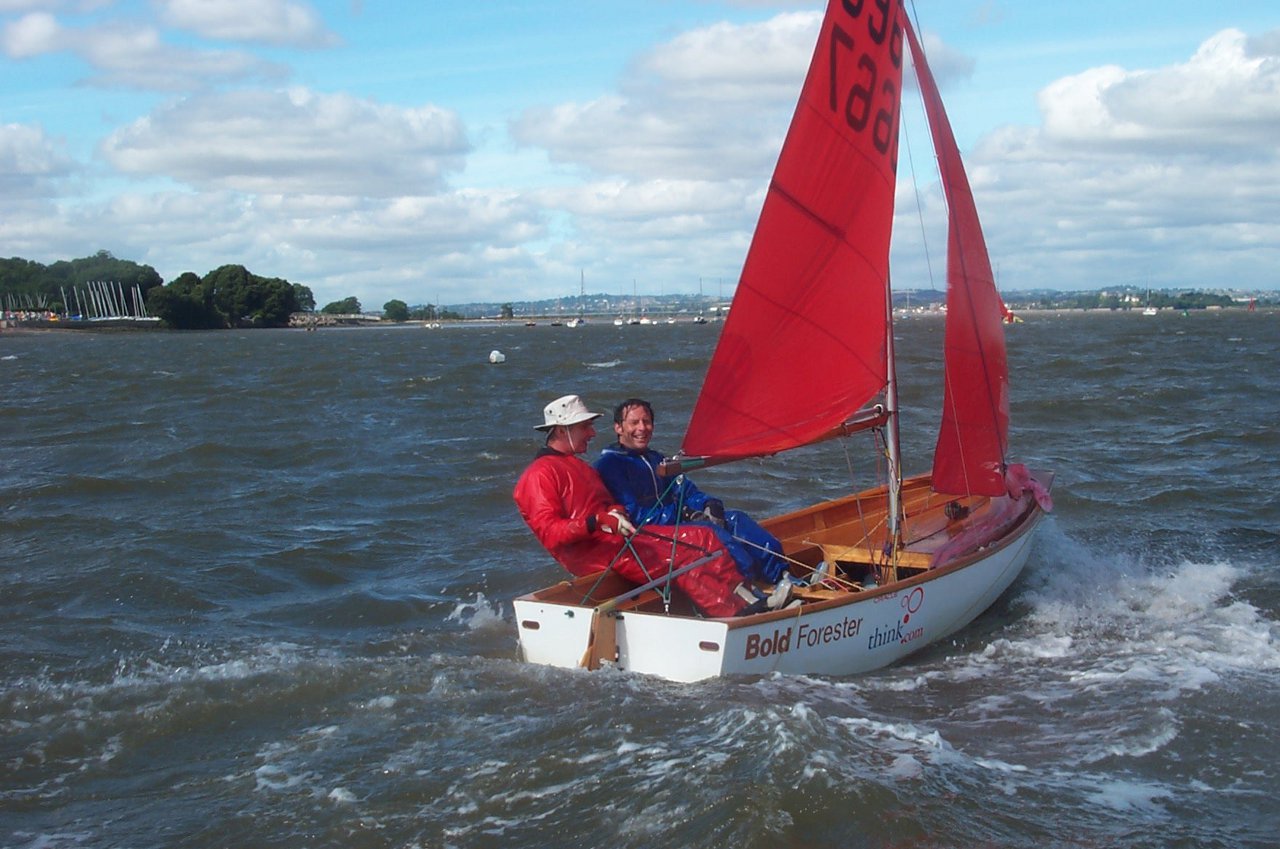Two men sailing a white wooden dinghy to windward in a force 5