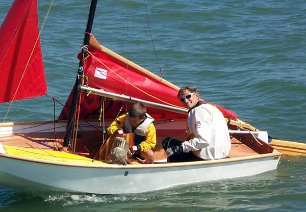 A white GRP composite Mirror dinghy being towed with mainsail down