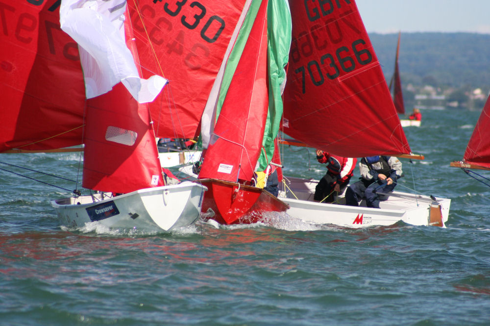 A fleet of Mirrors running close together with spinnakers flying sailing towards the camera and the leeward mark (out of shot) while others race past them to windward