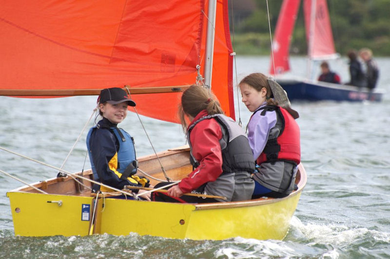 3 children sailing and chatting in a yellow Mirror dinghy