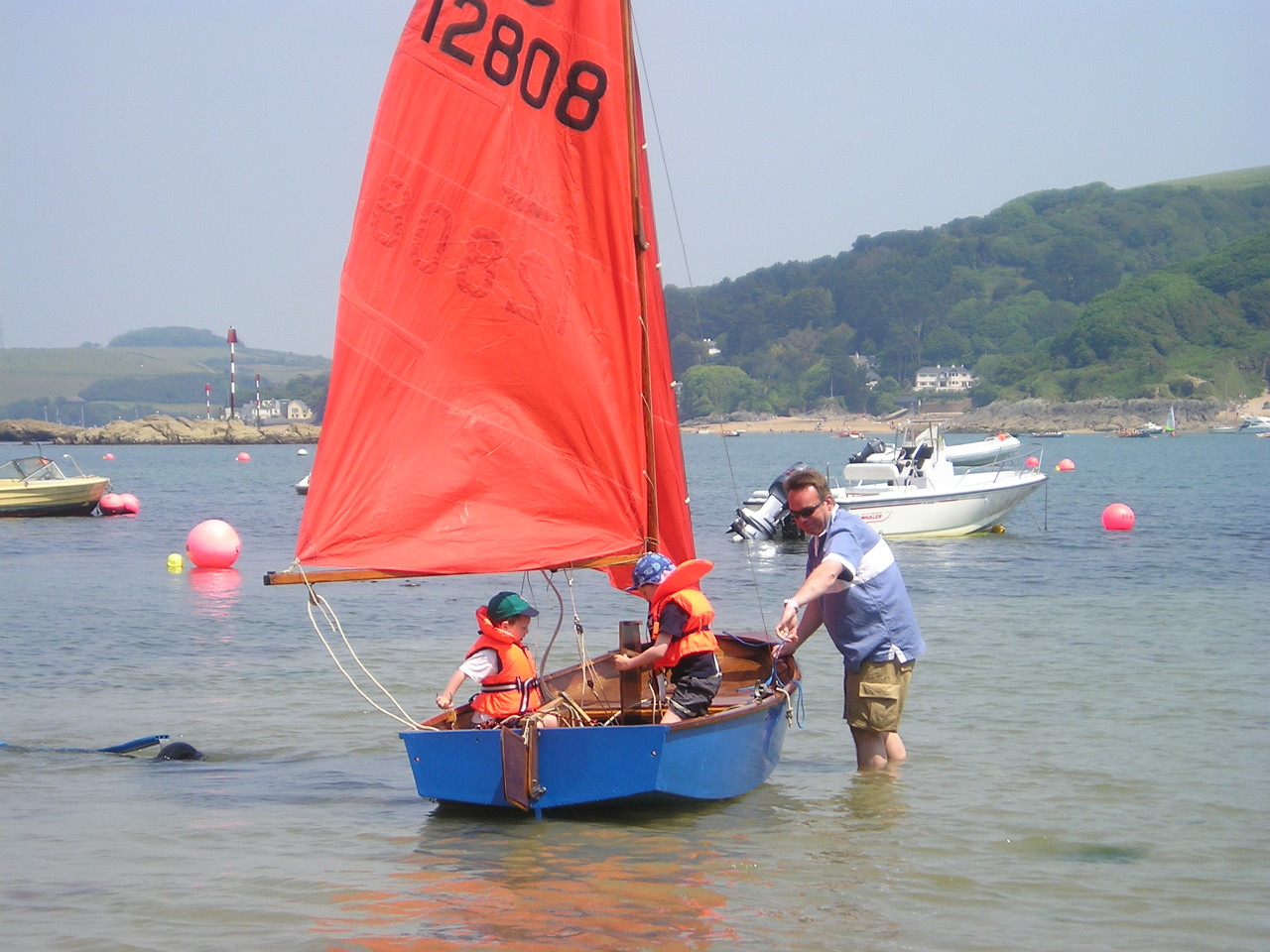 A blue wooden Mirror dinghy, with two small children aboard, getting ready to set sail