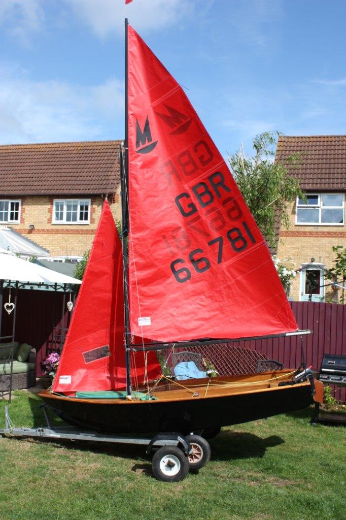 Black wooden Mirror dinghy rigged up in a garden