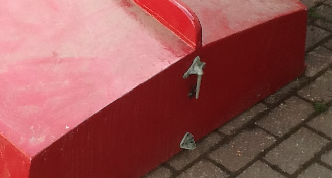 The rudder fittings on the aft transom of a red Mirror dinghy which is upside down on a driveway