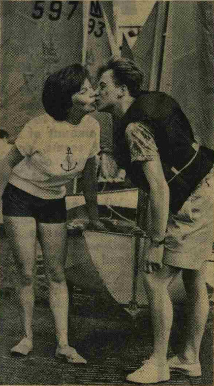 A couple kissing on the slipway with their rigged Mirror dinghy, and other Mirrors launching, in the background