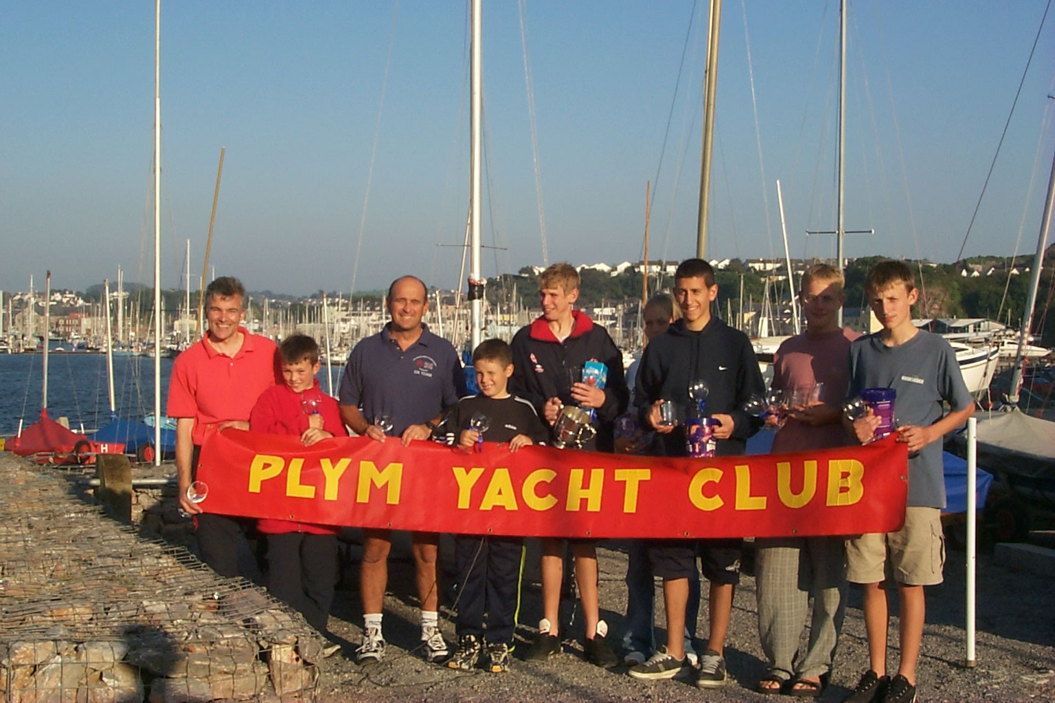 Prizewinning helms and crews behind a red banner with yellow lettering saying 'Plym Yacht Club'