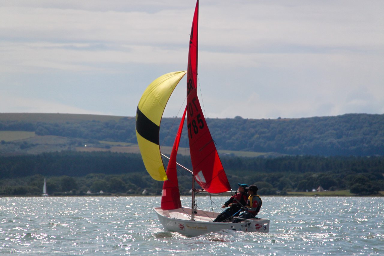 A white Mirror with yellow and black striped spinnaker sailing away from the camera