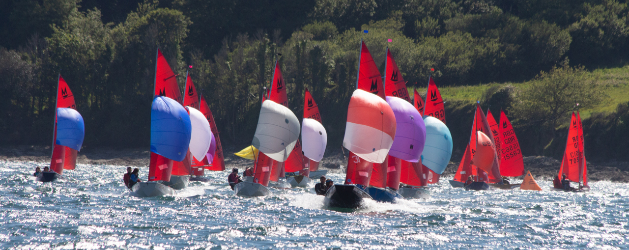 A fleet of Mirror dinghies with spinnakers set racing towards the camera on a broad reach