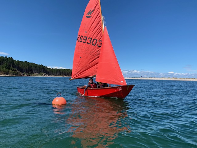 A red Mirror dinghy sailing on a loch on a bright sunny day