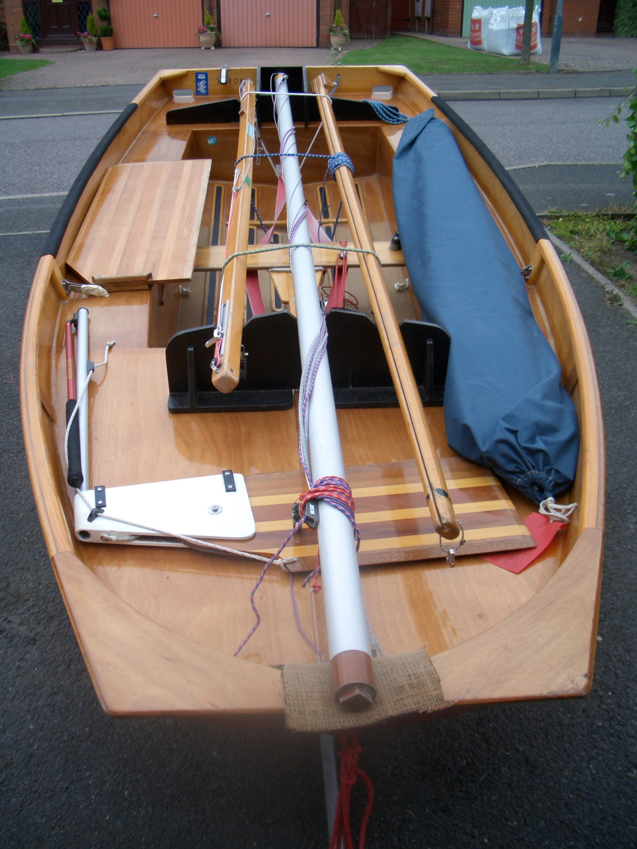 A red wooden Mirror dinghy with mast down on a driveway, bow towards the camera