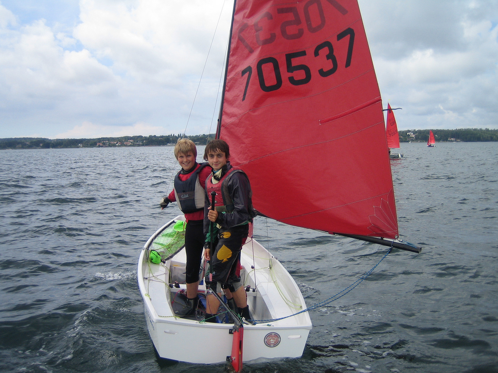 A white GRP Mirror dinghy with helm and crew standing up looking towards the camera