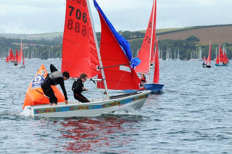 White Mirror dinghy, with 'Birthday Boy' banner around it,  hoisting spinnaker at the windward mark